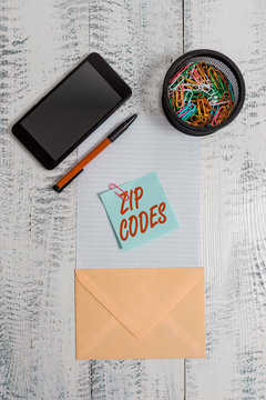Word writing text Zip Codes. Business photo showcasing numbers added to a postal address to assist the sorting of mail Smartphone paper sheet clips holder pen envelope note wooden background
