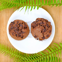 Chocolate birthday cupcakes with a cocoa frosting on top on a black plate with dessert cutlery, on a dark white background, horizontal
