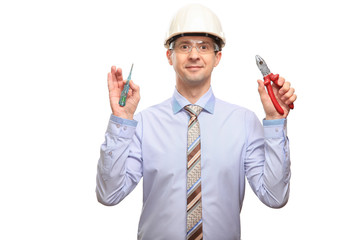 Satisfied man in a helmet, glasses, office shirt and tie holds hand tools, isolated