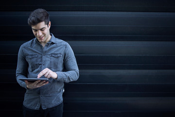 Portrait of young handsome caucasian man typing on tablet computer and surfing internet. Copy space.