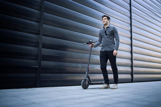 Shot Of Young Handsome Caucasian Man Standing By His Electric Scooter On The Street.