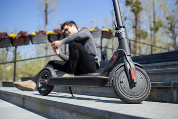Naklejka premium Electric scooter commuting vehicle and young man sitting in background using smart phone.