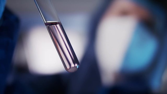 Laboratory analisys and research. Female laborant in protective suit researching sample in glass tube