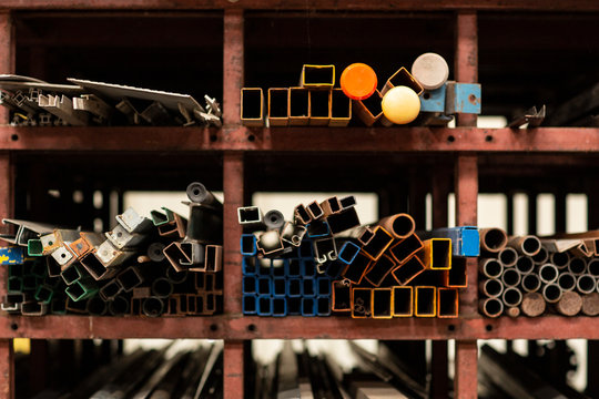 A Detail Of Different Styles And Sizes Of Old Recycled Metal Pipes And Profiles, Construction Materials Laying On A Shelf Rack In A Storage. Recycled Metal Pieces, Circular Economy Principle