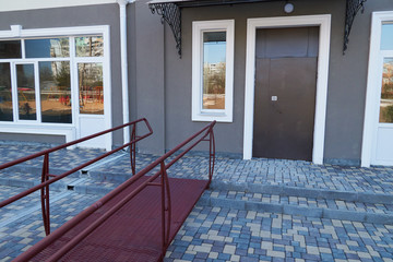 Wheelchair access ramp for entrance of residential multistory building, city street and tiles sidewalk