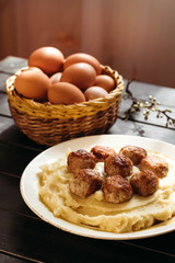 Composition of mashed potatoes with fried meatballs and eggs on dark background.