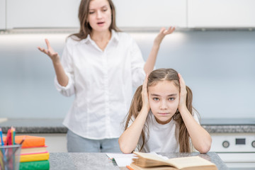 Sad teen girl covers her ears while her mother scolds her for poor study. Family relationships