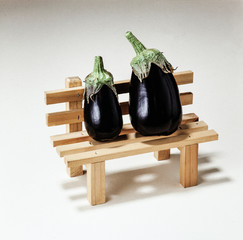 Two black eggplants on a wooden bench against a white background