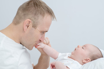 Happy father kisses hand his newborn baby on the bed at home