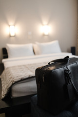 black travel leather bag on the nightstand against the background of the bed in the hotel room