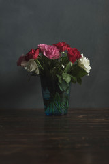 Vase with red, pink and white roses on a wooden table.