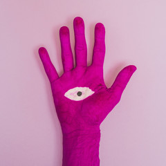 Painted in fuchsia pink hand with a drawn eye in the middle of the palm on a light purple or lilac background. Abstract modern minimal pop art.