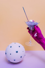 The witch's pink painted hand holds a potion or cocktail with a unicorn horn instead of a straw near a fortune telling ball with many eyes.