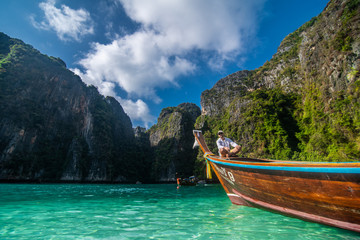 Plakat Handsome male cruising on retro wood boat by Andaman sea and behind him you can see Ko Phi Phi Lee Island.