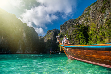 Handsome man tourist, sitting on a boat with blue turquoise sea water, on blue lagoon of Phi phi...