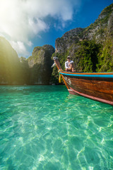 Handsome male cruising on retro wood boat by Andaman sea and behind him you can see Ko Phi Phi Lee Island.