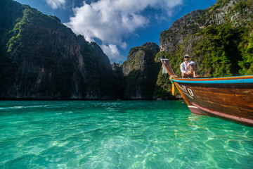 Handsome man tourist, sitting on a boat with blue turquoise sea water, on blue lagoon of Phi phi island in summer season during travel holidays vacation trip.