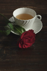 White china tea cup and saucer with red rose on wooden table.