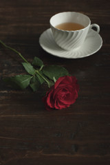 White china tea cup and saucer with red rose on wooden table.