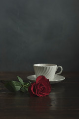 White china cup and saucer with red rose on wooden table.