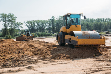 yellow asphalt paver compactor working on sand at a construction site
