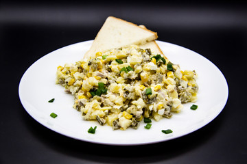 Ukrainian and Russian salad Olivier according to a new recipe on a white plate. Healthy salad Olivier with meat, corn and slices of white bread. Delicious and tasty salad on white plate.