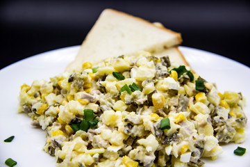 Ukrainian and Russian salad Olivier according to a new recipe on a white plate. Healthy salad Olivier with meat, corn and slices of white bread. Delicious and tasty salad on white plate.