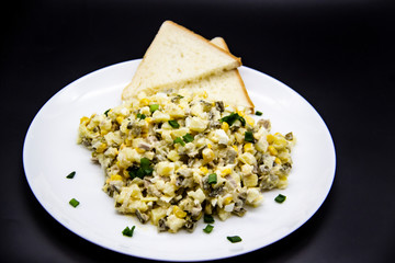 Ukrainian and Russian salad Olivier according to a new recipe on a white plate. Healthy salad Olivier with meat, corn and slices of white bread. Delicious and tasty salad on white plate.