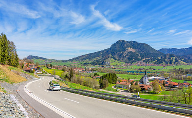 Country road with car and Gruenten mountain in spring. Allgäu, Bavaria, Germany