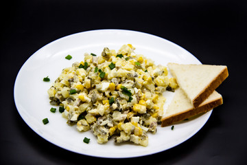 Ukrainian and Russian salad Olivier according to a new recipe on a white plate. Healthy salad Olivier with meat, corn and slices of white bread. Delicious and tasty salad on white plate.