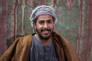 Portrait of Bedouin man wearing traditional clothes praying with a tasbih while drinking tea on a carpet in the Saudi desert