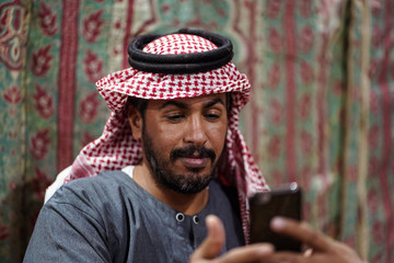 Fototapeta na wymiar Bedouin man wearing traditional headscarf looks himself in his smartphone in the Saudi desert