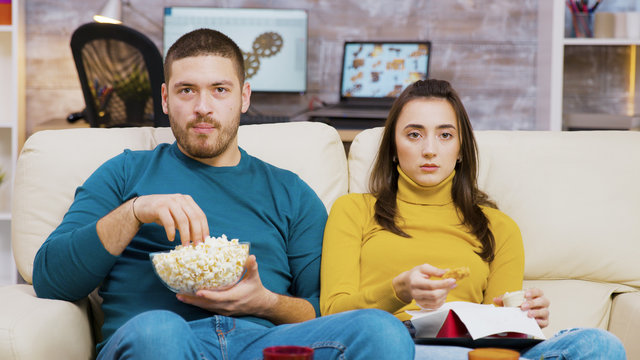 Scared Couple Watching Tv Eating Pizza And Popcorn Sitting On Couch