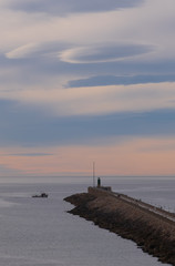Long pier at sunset with beautiful clouds. Lighthouse and a small fishing boat in the distance