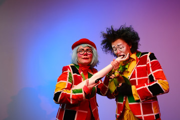 Two clowns a man and a woman with makeup in bright colored costumes are fooling around and showing a presentation