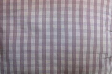 Close-up on the fabric of a pillow. it is made up of a repetitive geometric pattern of small tiles in different shades of gray. The lines formed are perpendicular to each other.
