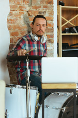 Fototapeta premium Caucasian musician playing drumms during online concert at home isolated and quarantined. Using camera, laptop, streaming, recording courses. Concept of art, support, music, hobby, education.