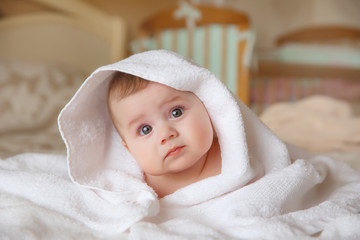 baby is wearing diapers and a white towel in bedroom. A newborn baby is resting in bed after a bath or shower. Children's room. Textiles and bedding for children.