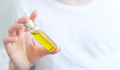The girl holds in her hand a transparent bottle with oil on a light background. Aromatic oil, essential oil. Close-up. Space for text. Mockup