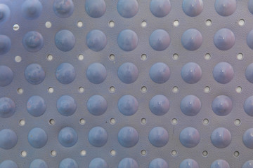 Close-up of a blue plastic bath mat made of bubbles and holes to prevent skidding. It is glued to the wall and lit with natural light. the patterns are geometric and repetitive