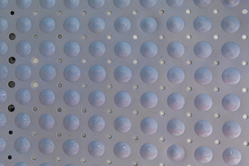 Close-up of a blue plastic bath mat made of bubbles and holes to prevent skidding. It is glued to the wall and lit with natural light. the patterns are geometric and repetitive