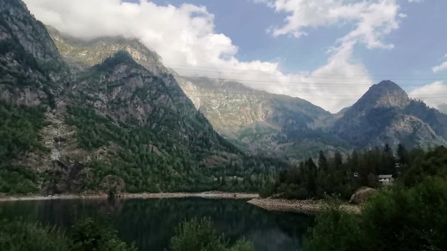 moving forward to pine woods forest lake and mountain valley with sun flare in summer day. Europe Italy Alps outdoor green nature scape mountains wild aerial establisher.