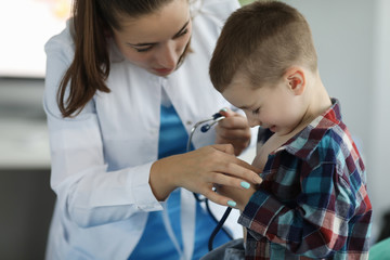 Close-up of friendly pediatrician entertaining kid and examine lugs with stethoscope. Happy and lovely atmosphere in clinic office. Medicine and healthcare concept