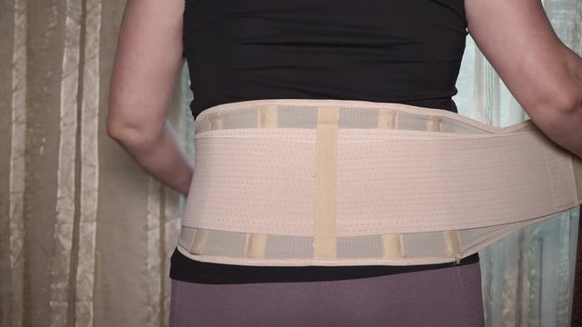 The girl at the window puts an orthopedic corset on her lower back