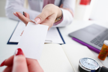 Female physician hand give white blank calling card to businesswoman closeup in office. Physical disease prevention examine patient instrument shop healthy lifestyle family doctor concept