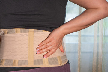 A woman sitting on a sofa in a orthopedic support corset. Posture corrector for back and spine