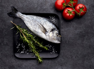 Dorado fish on the black stone with  rosemary  and tomatoes. Top view.