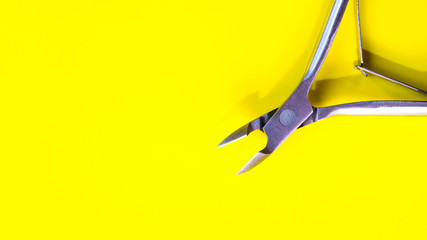 Manicure tool on a yellow background. Steel tweezers to remove cuticles. Hand and nail care, manicure. Cosmetic procedures for both women and men. Copy space, place for text. Flat lay. Top view.