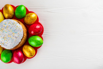 Easter cake kulich. Traditional Easter sweet bread and easter colorful eggs on plate on white wooden background. Copy space.