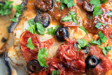 Slices of swordfish with cherry tomatoes, black olives and parsley.